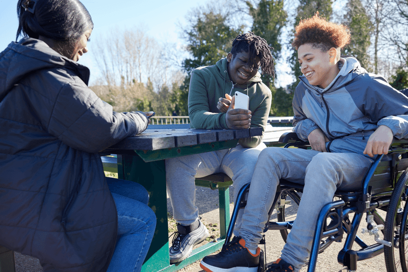 Teenage Girl In Wheelchair With Friends Looking At Social Media On Mobile Phones In Park - stock photo
Teenage Girl In Wheelchair With Friends Looking At Social Media On Mobile Phones In Park